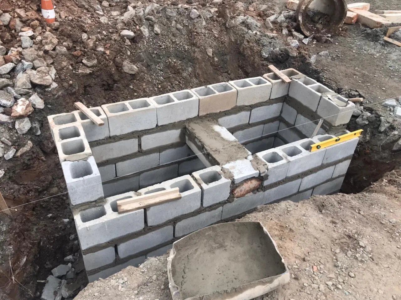 Boca de lobo em construção, com blocos de concreto assentados dentro da vala